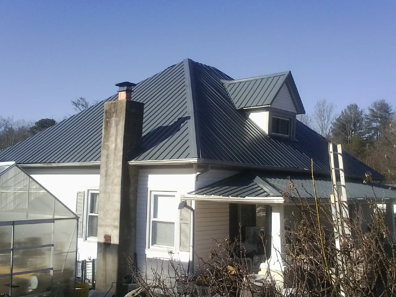Dark blue standing seam metal roof on a white farmhouse with dormer — Slate & Tile Roof Repair by Roofing Brothers in Kemmerer