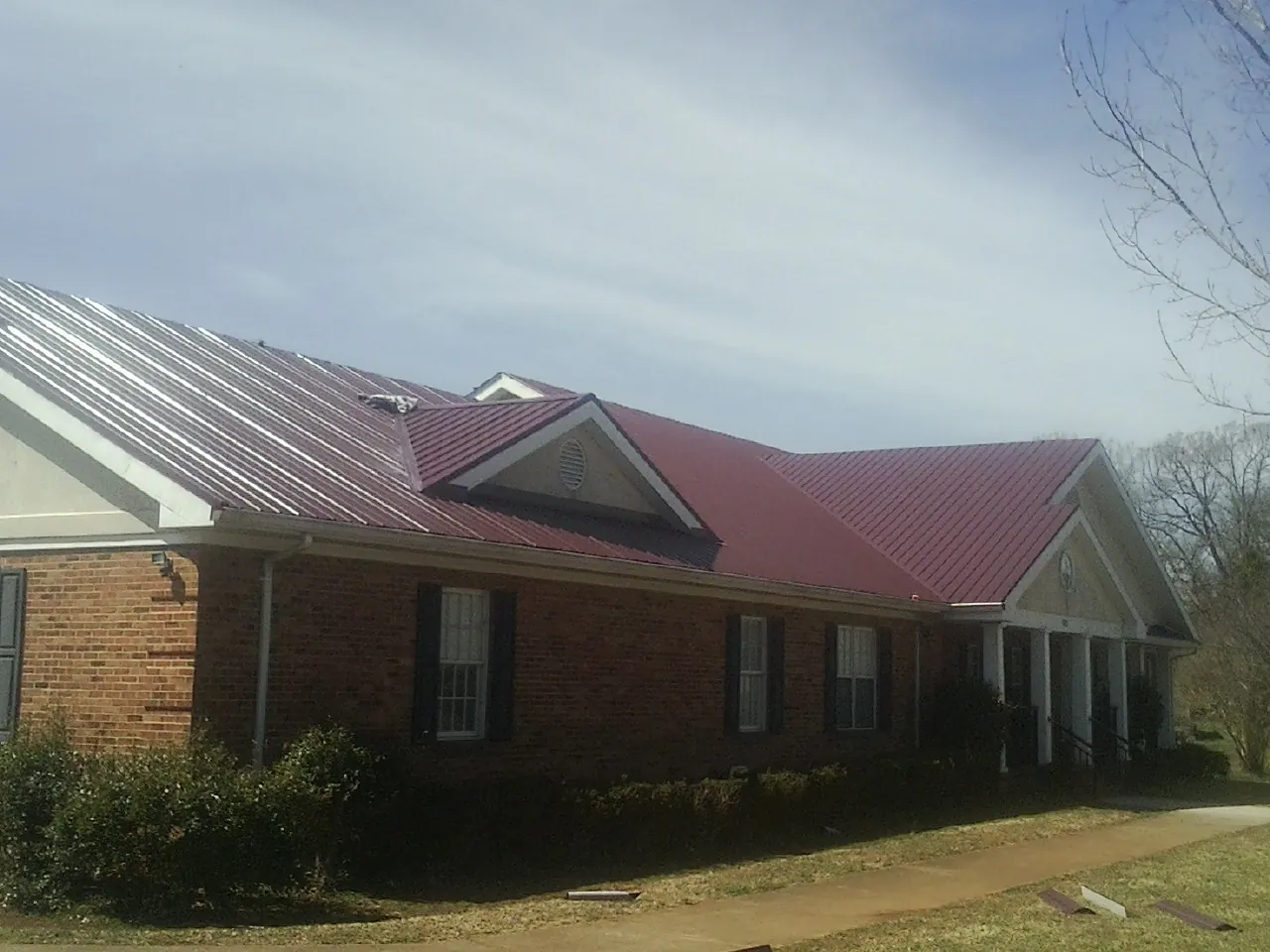 Red metal roof with gabled entries on a long brick building, from a Hail Damage Roof Repair job in Kemmerer