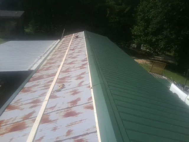 Old rusted panels beside newly installed green metal roofing — Wind Damage Roof Repair by Roofing Brothers in Kemmerer