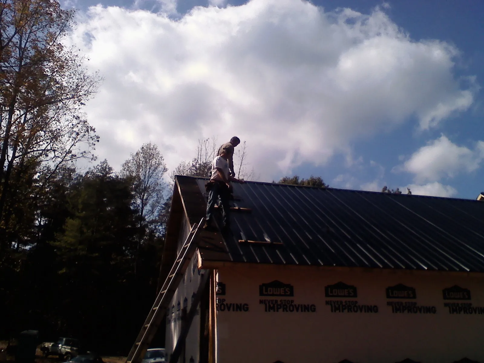 Roofer fastening dark metal panels high against a cloudy sky, from a Roof Inspection job in Kemmerer